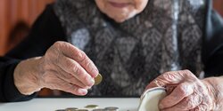 Elderly woman sitting at the table counting money in her wallet. - 1